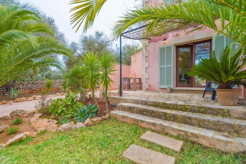 Una casa rosa da a un patio ajardinado con escalones de piedra y plantas tropicales.
