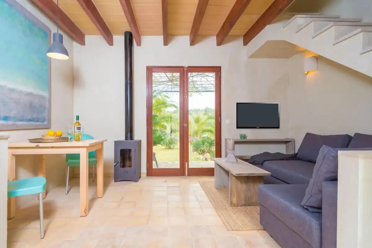 Una sala luminosa con asientos, una mesa de comedor y puertas de vidrio frente a la vegetación.