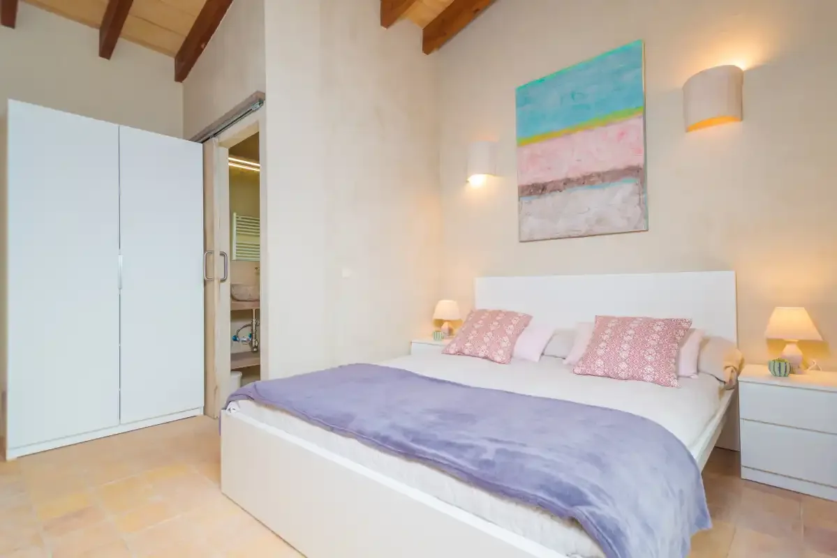 Un dormitorio con una cama, almohadas rosas y una obra colorida sobre el cabecero.