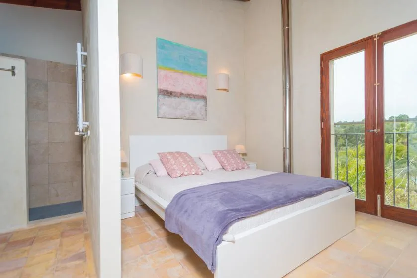 Un dormitorio con una cama, arte colorido en la pared y puertas de vidrio hacia un balcón.