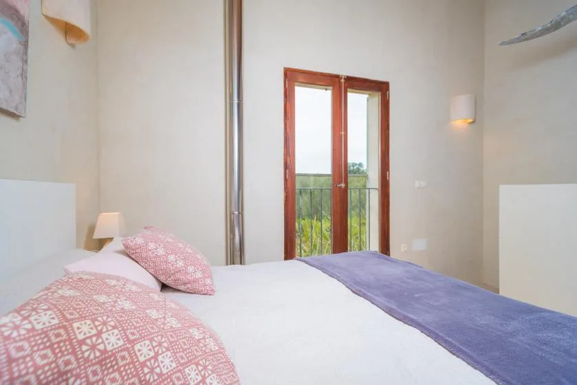 Un dormitorio con una cama, almohadas estampadas y puertas de cristal que dan a un balcón.