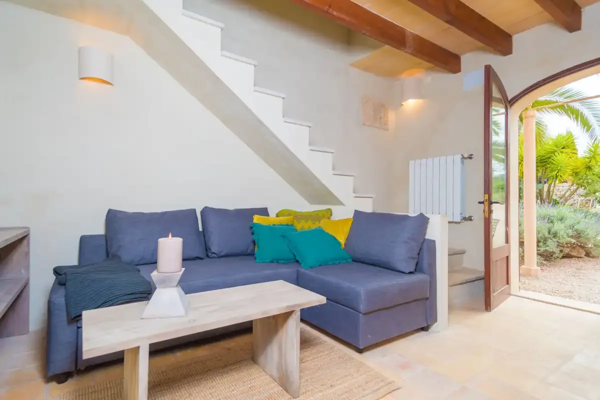 Una sala de estar con asientos azules bajo una escalera y una puerta abierta al jardín.
