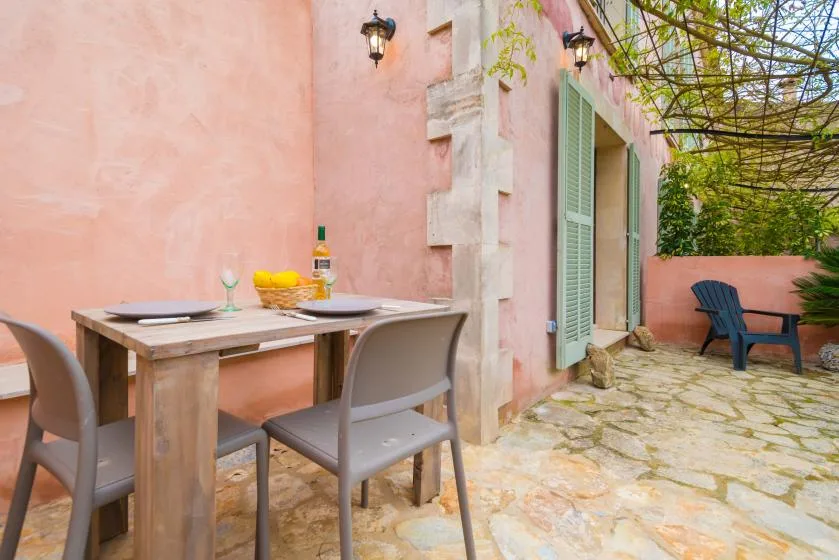 Un patio de piedra con una mesa de comedor y asientos junto a una pared rosa.