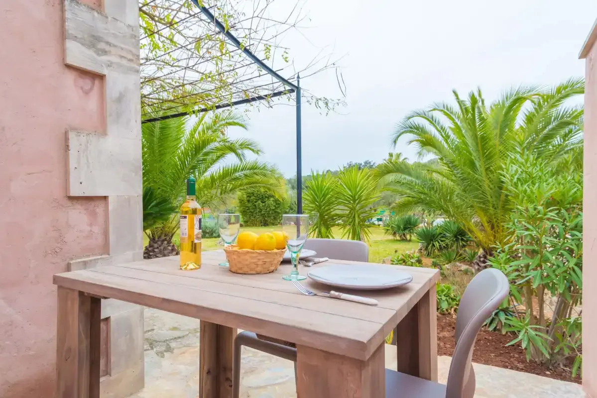 Una mesa de comedor en el patio da a un jardín con palmeras y vegetación.