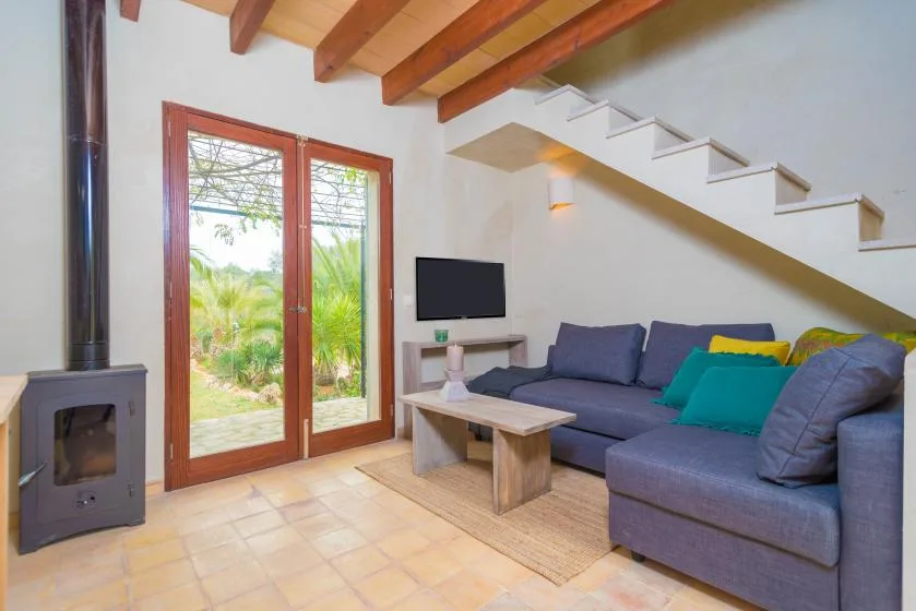 Sala de estar con asientos, un televisor y puertas de vidrio que dan a la vegetación.