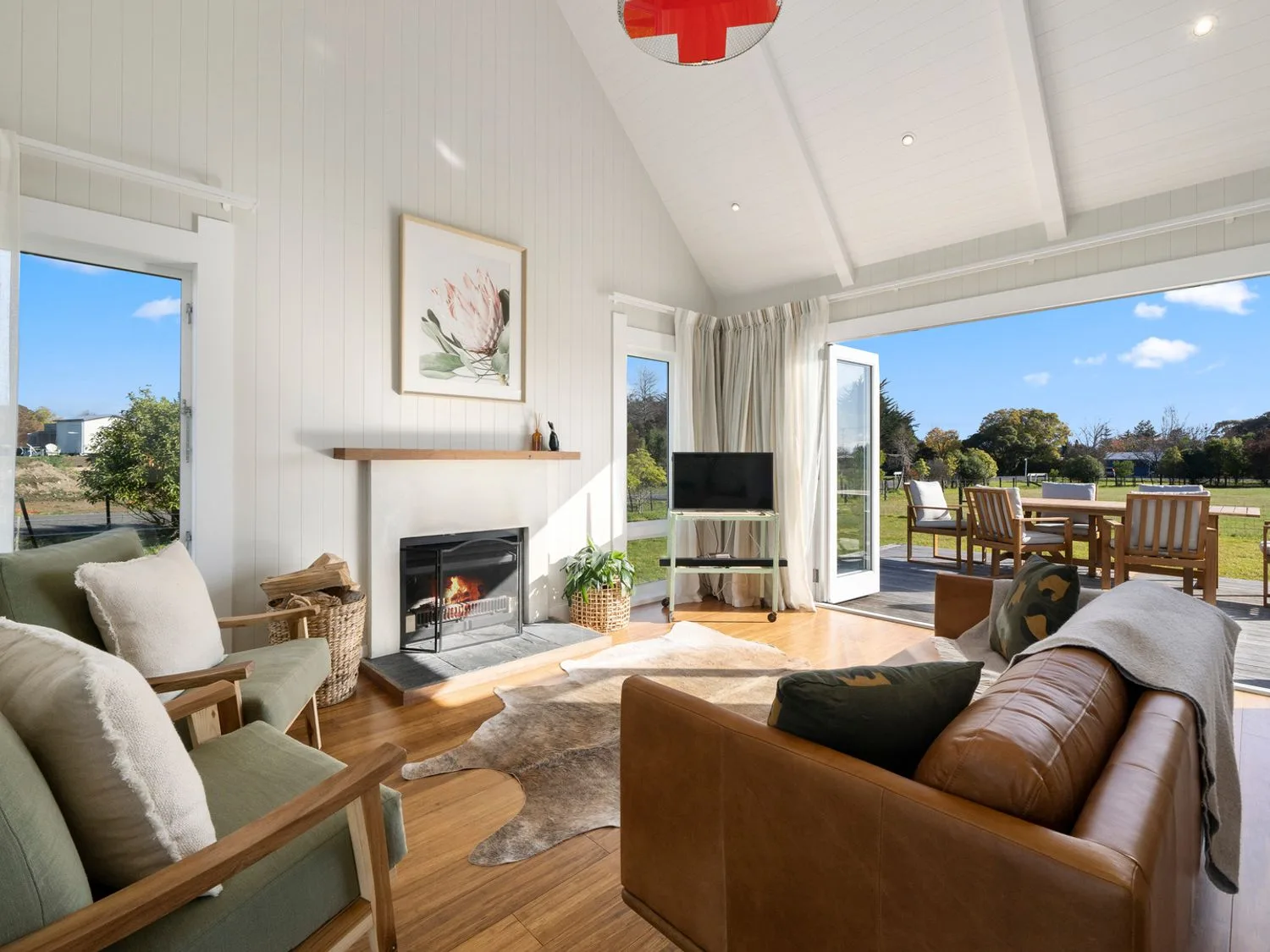 Una sala de estar con chimenea y puertas abiertas a un patio con comedor al aire libre en Te Whare Hipi - Martinborough Holiday Home, en Martinborough.