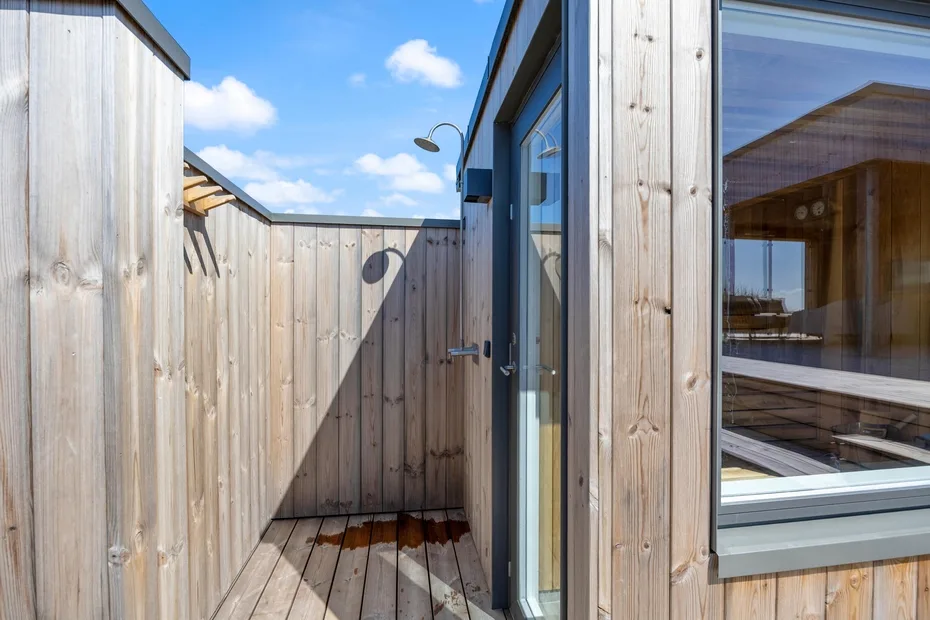 Una ducha exterior revestida de madera junto a una puerta de vidrio y una ventana.