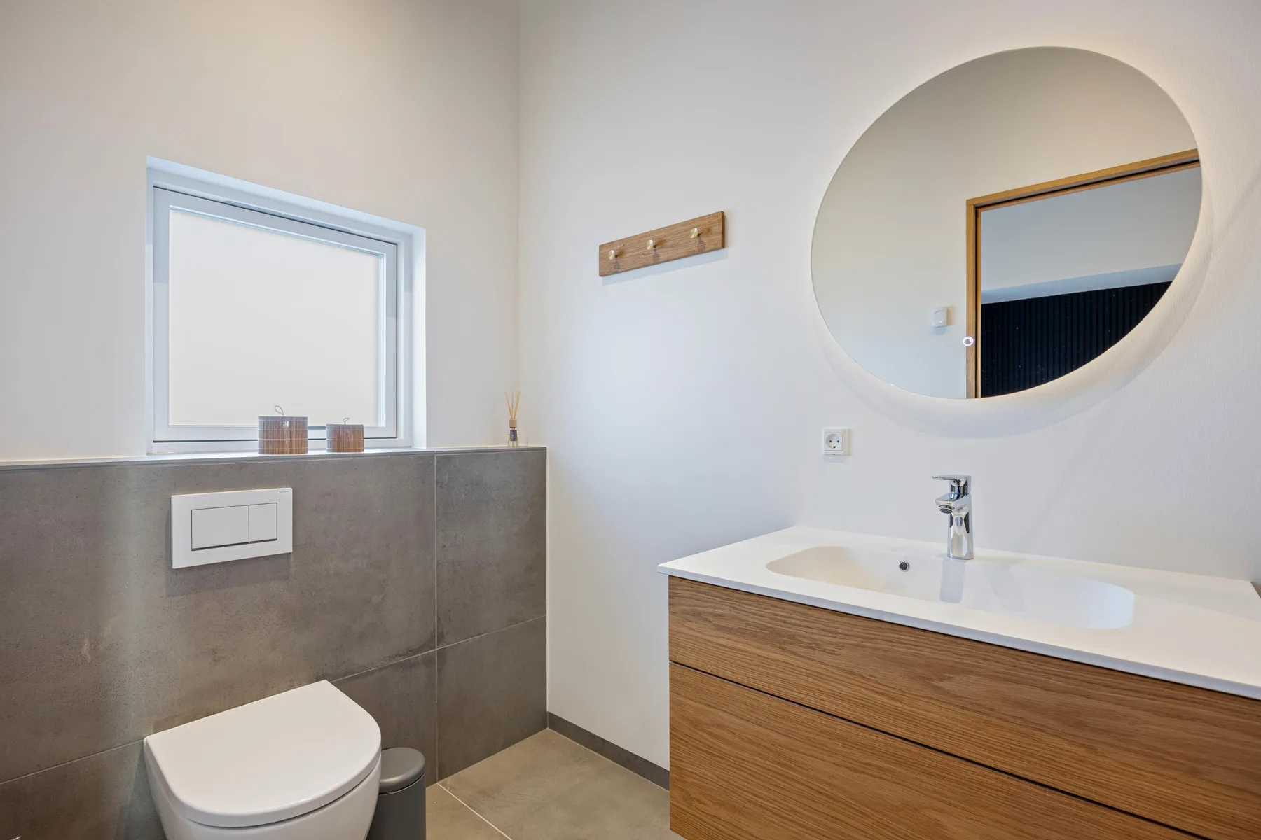 Un baño luminoso con mueble de madera, espejo de pared e inodoro.