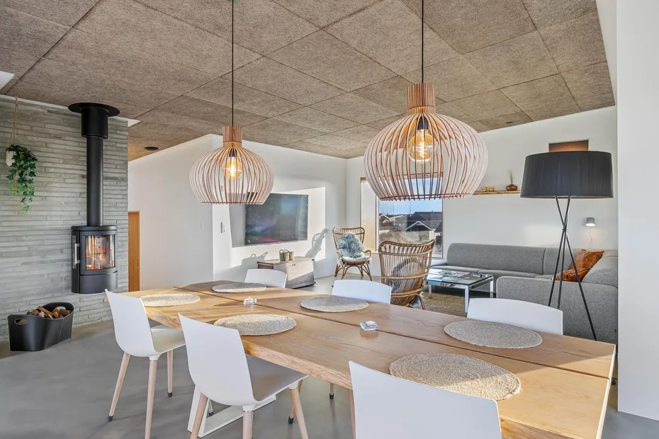 Un comedor y sala de estar con una mesa larga y lámparas colgantes.