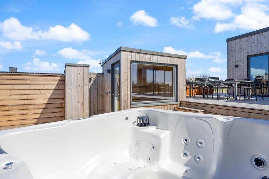 Una bañera de hidromasaje al aire libre está junto a una terraza de madera con asientos.