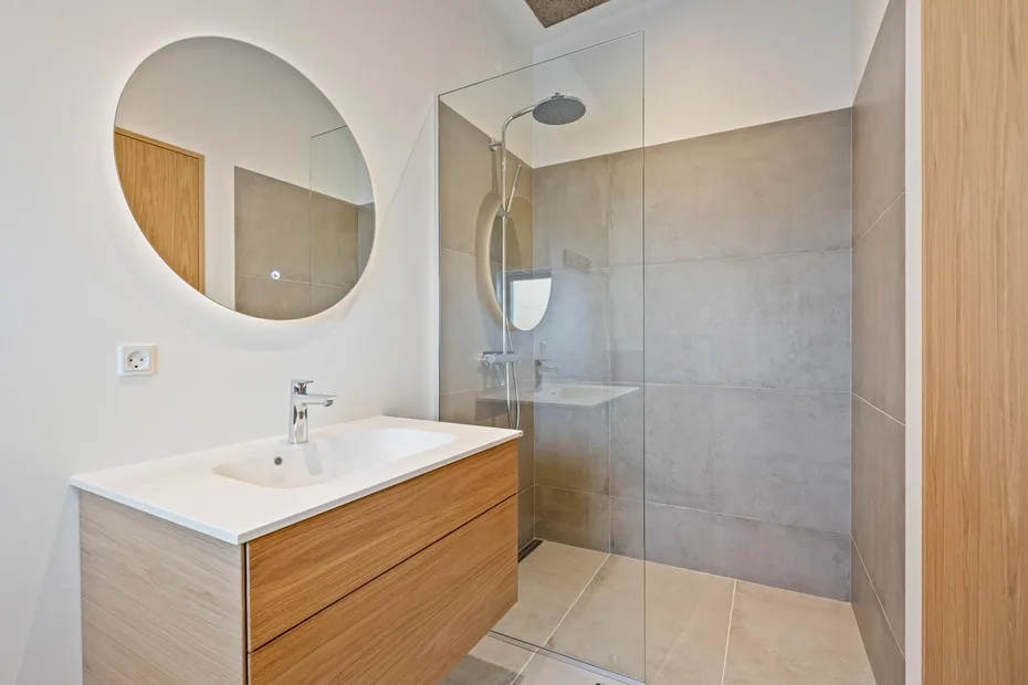 Un baño moderno con lavabo de frente de madera y ducha de vidrio.
