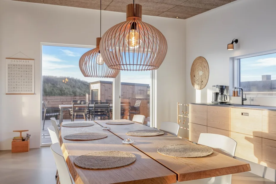 Un comedor luminoso con una larga mesa de madera y grandes lámparas colgantes.
