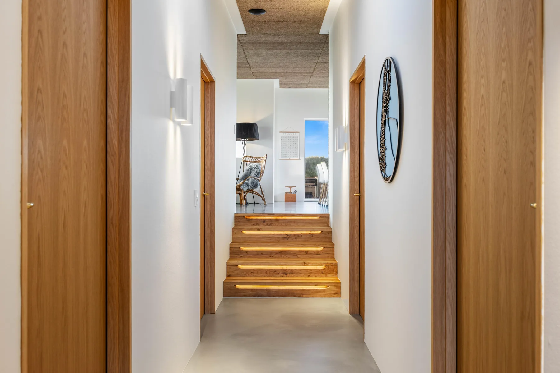 Un pasillo luminoso conduce a una zona elevada con asientos, escalones de madera y puertas.