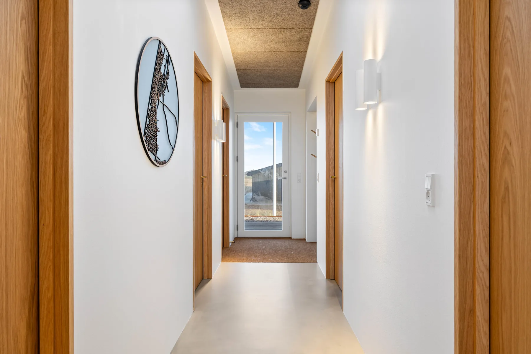 Un pasillo luminoso con puertas de madera y una puerta de vidrio al fondo.