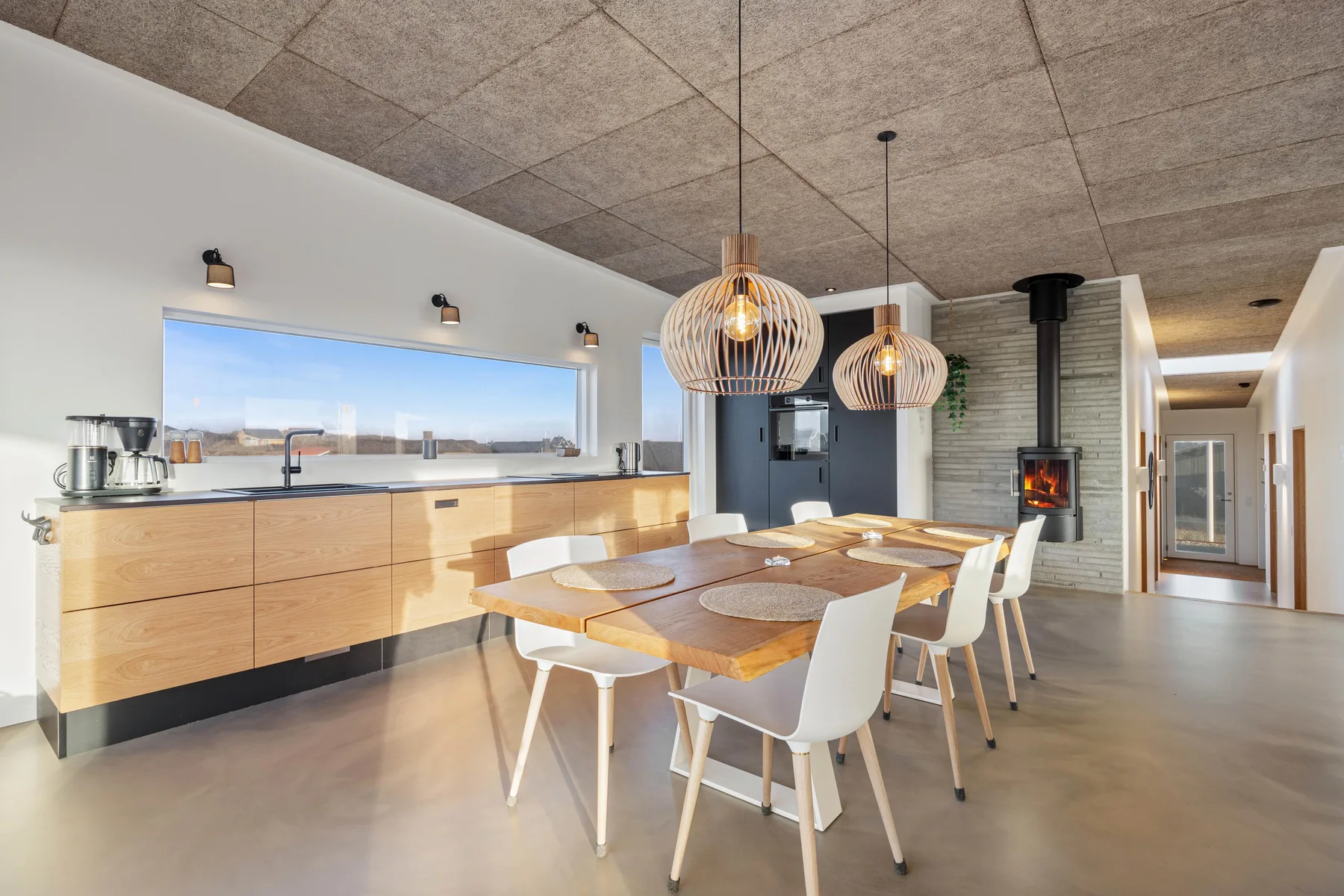 Comedor con una larga mesa de madera junto a una encimera de cocina y una ventana amplia.