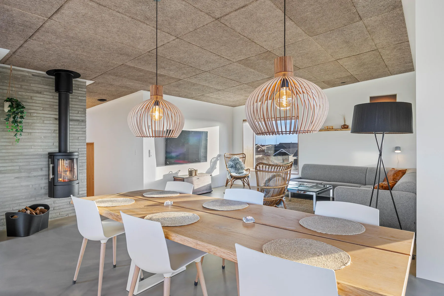 Comedor con una mesa larga de madera y lámparas colgantes junto a una sala de estar.
