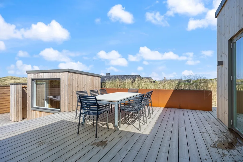 Una terraza exterior tiene una mesa de comedor y asientos junto a una estructura de madera.