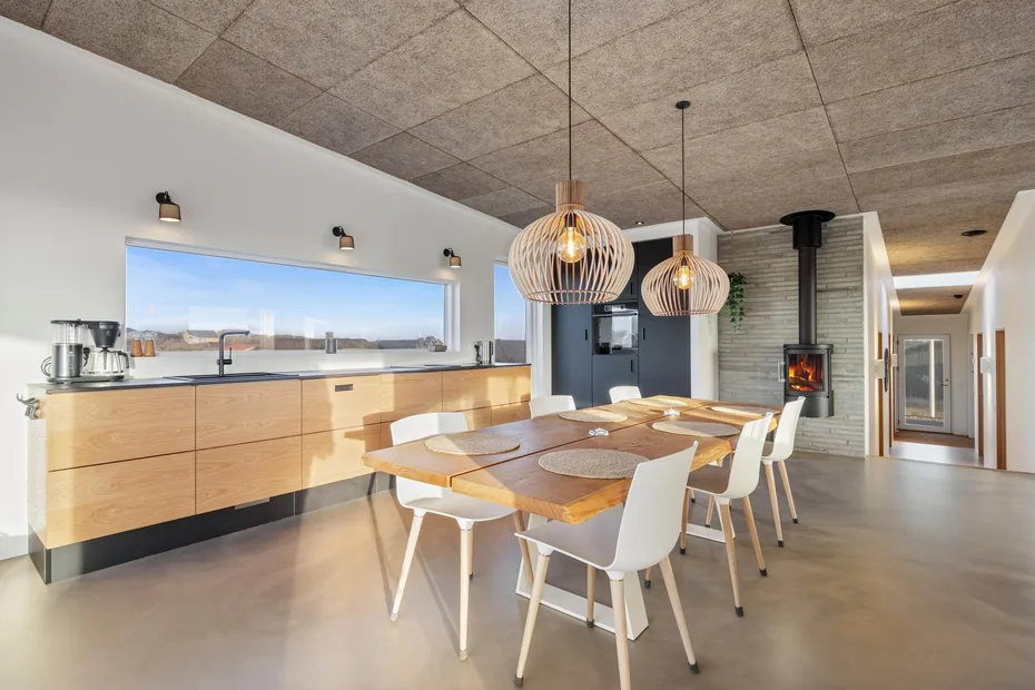 Una cocina abierta con zona de comedor y una mesa larga bajo lámparas colgantes.