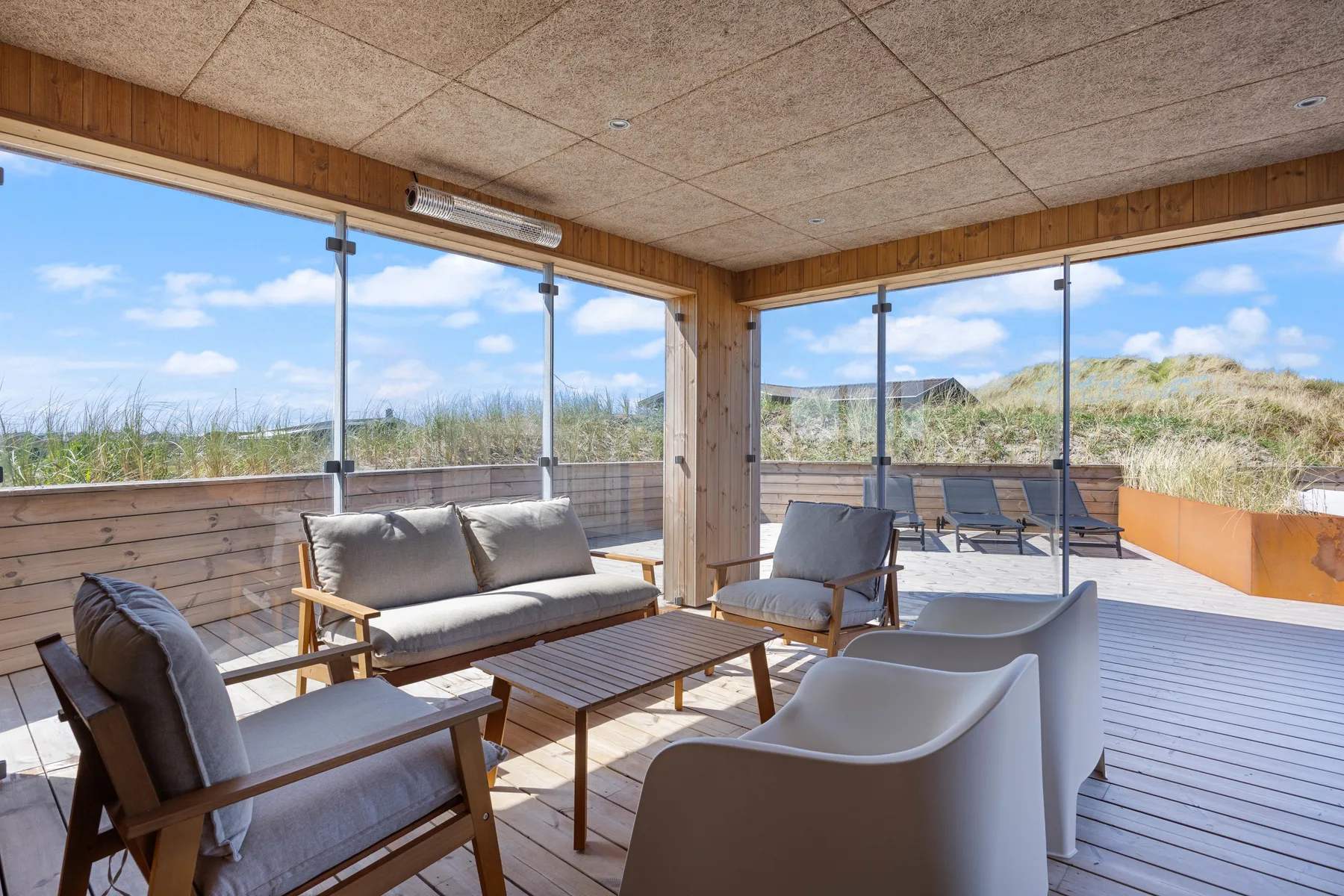 Una zona de estar en la terraza con una mesa de madera da a dunas cubiertas de hierba y al océano.