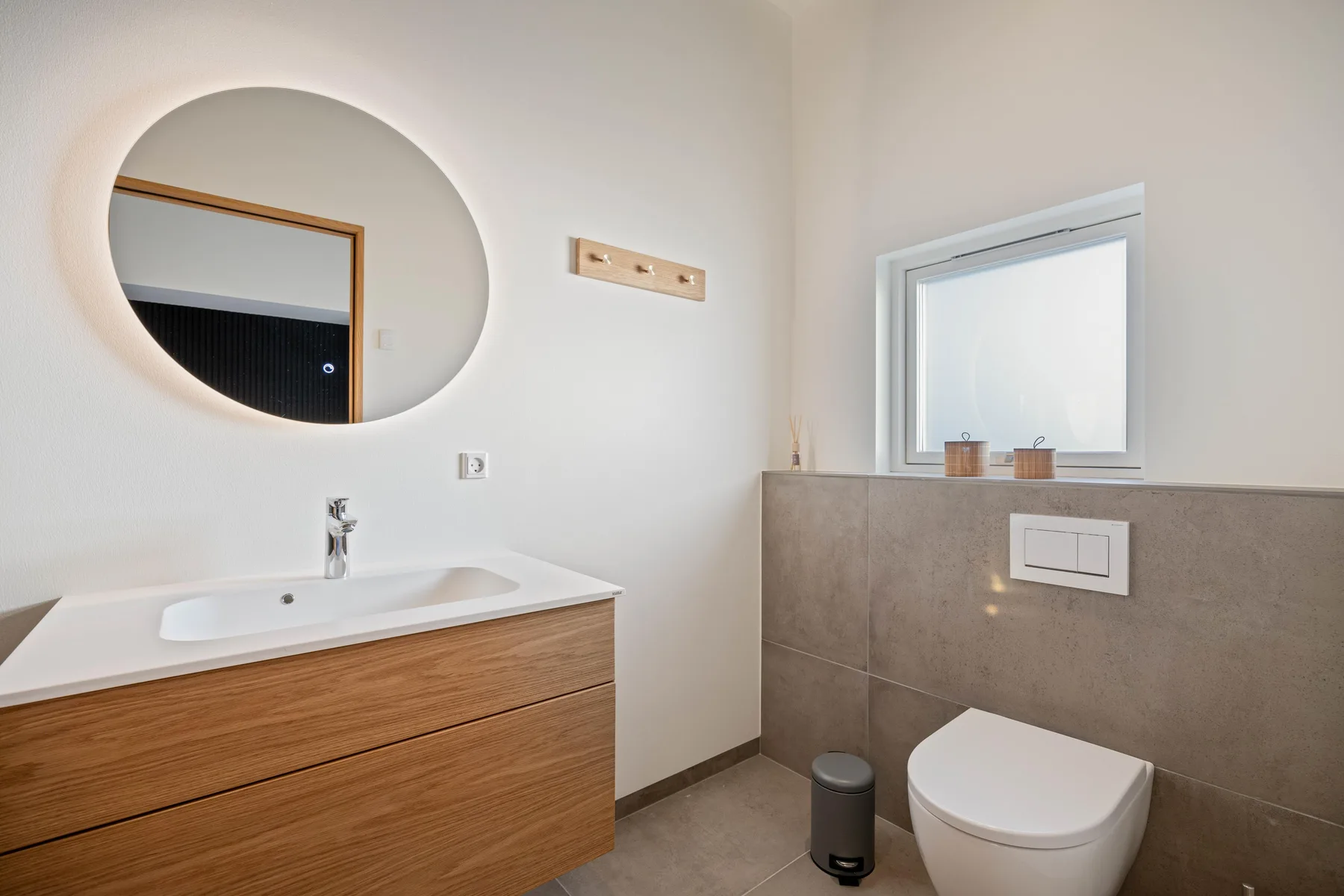 Un baño moderno con lavabo de frente de madera, espejo redondo e inodoro.