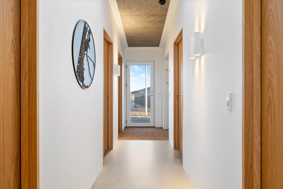 Un pasillo luminoso con marcos de madera y una puerta de vidrio al fondo.