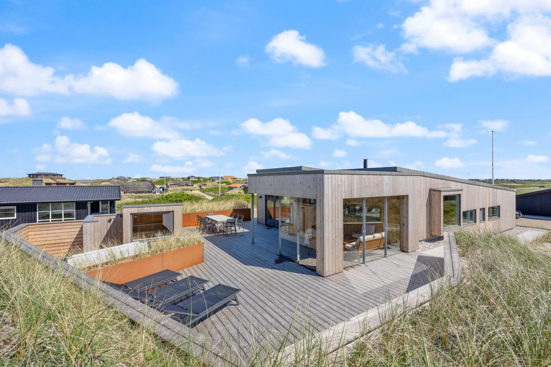 Una casa moderna con una amplia terraza de madera y asientos al aire libre.