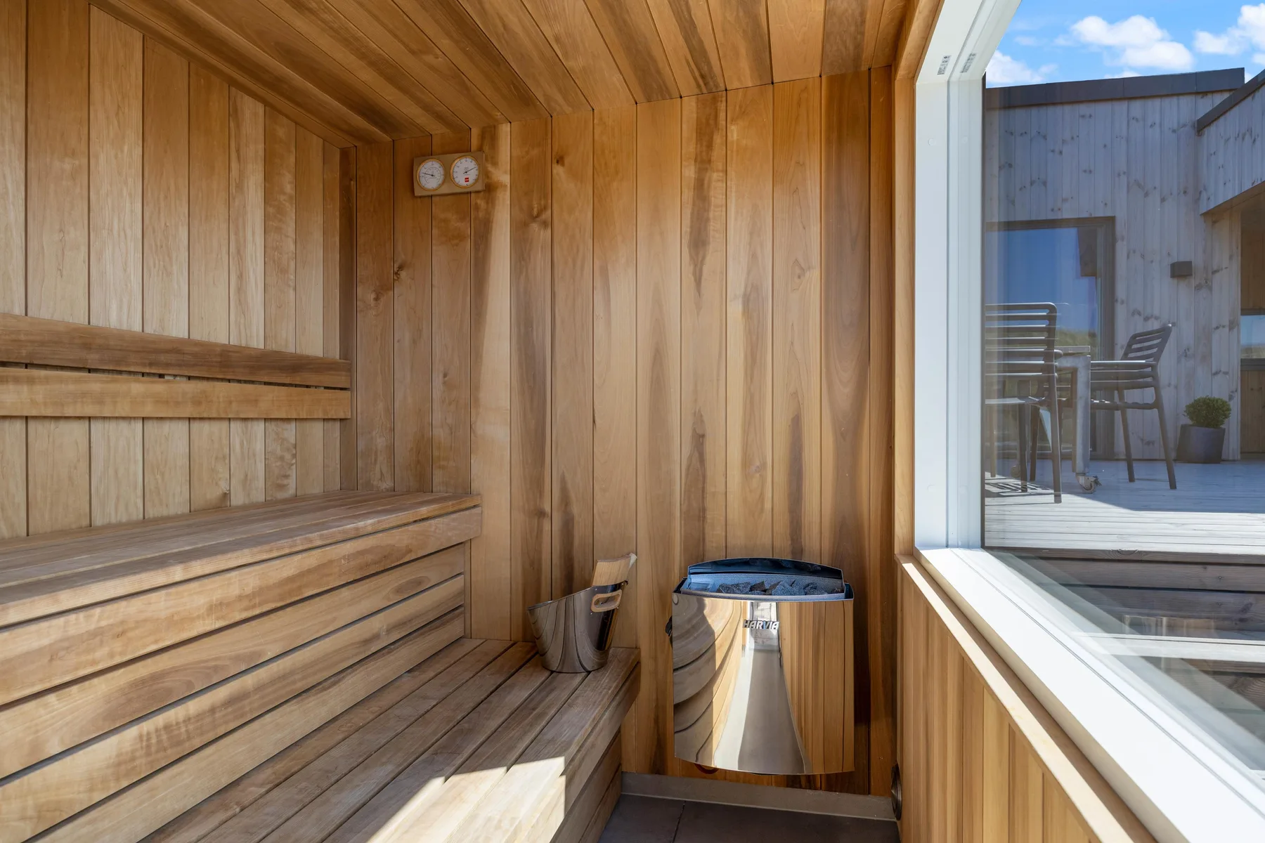 Una sauna revestida de madera, con bancos escalonados y un calentador junto a una ventana.