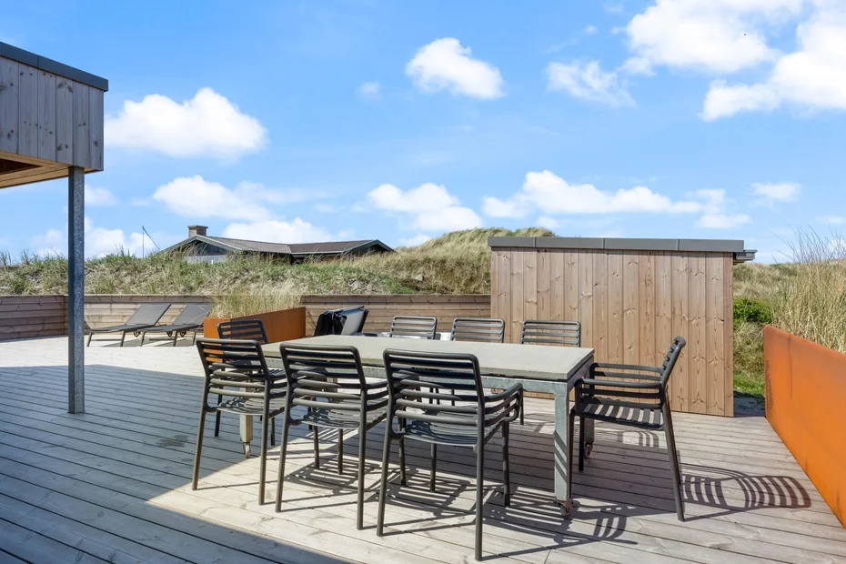Una terraza exterior tiene una mesa de comedor y asientos junto a una pantalla de madera.