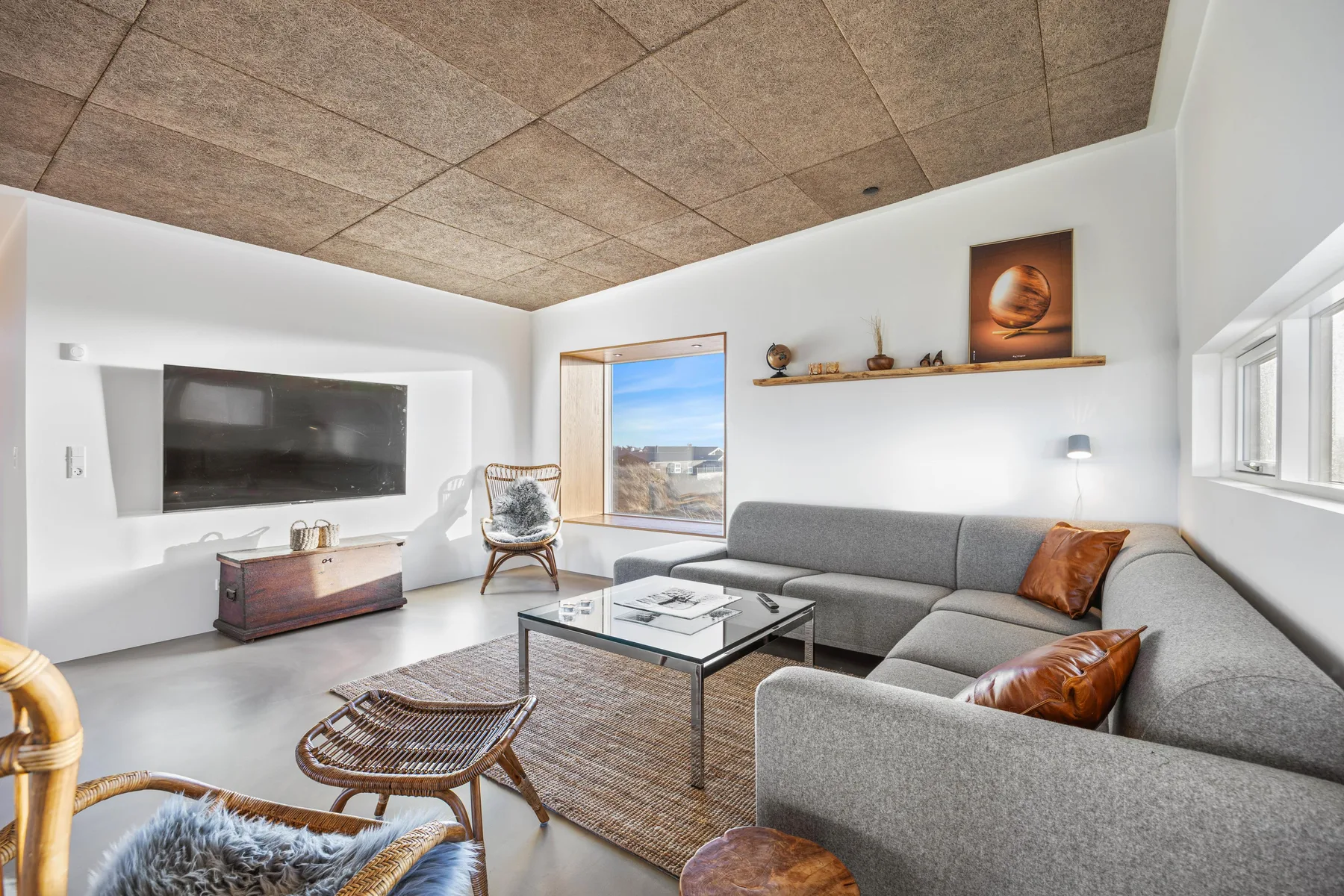 Una sala luminosa con asientos grises, una mesa de centro y ventanas grandes.