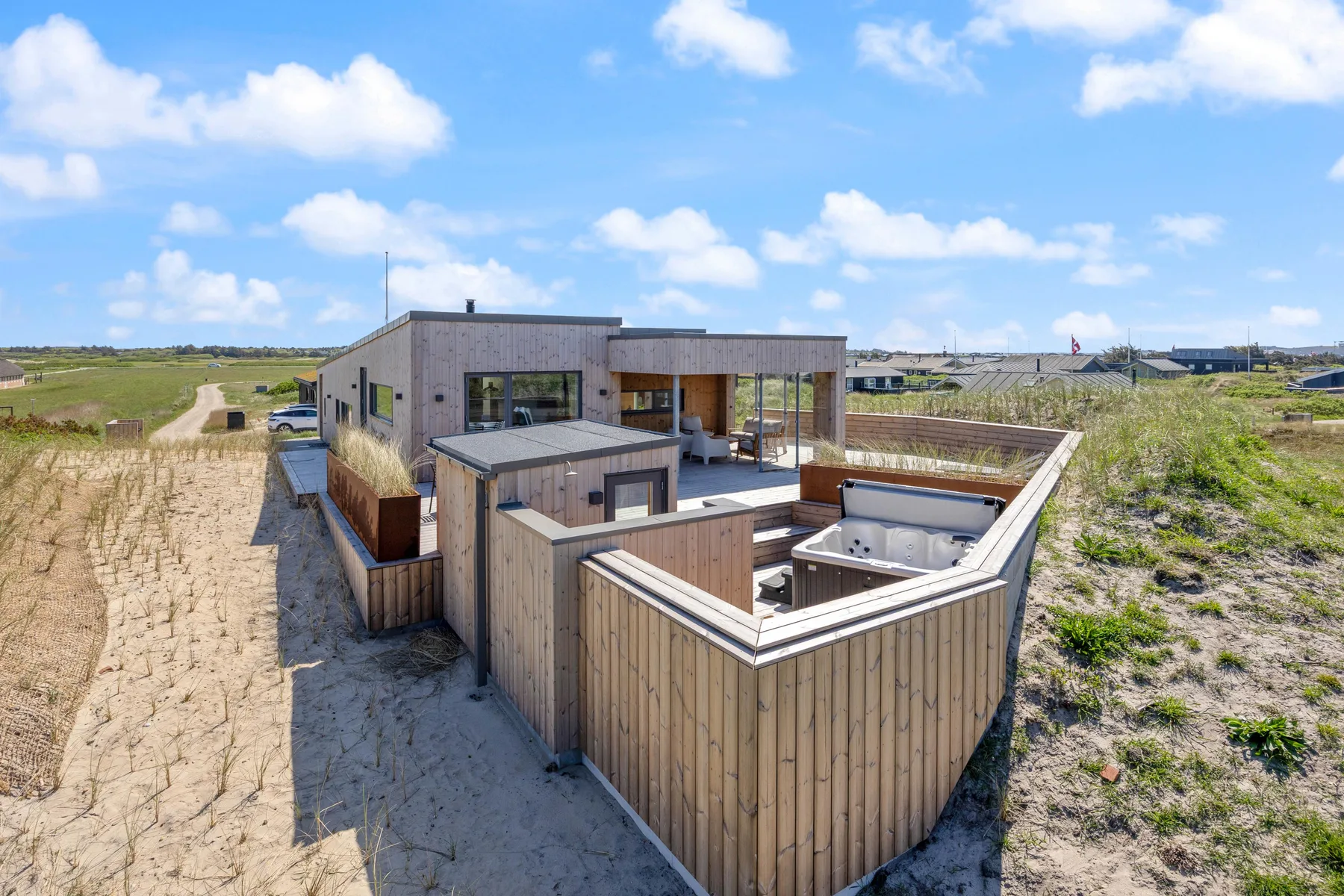 Una casa moderna con una bañera de hidromasaje exterior se encuentra en un paisaje arenoso abierto.