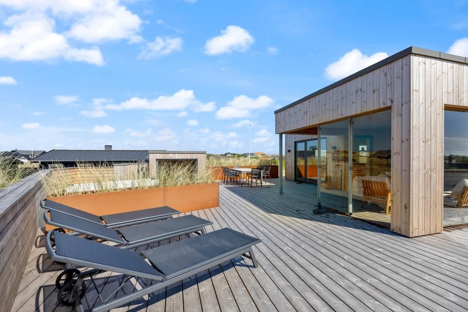 Una terraza en la azotea con asientos al aire libre junto a una estancia moderna con fachada de vidrio.