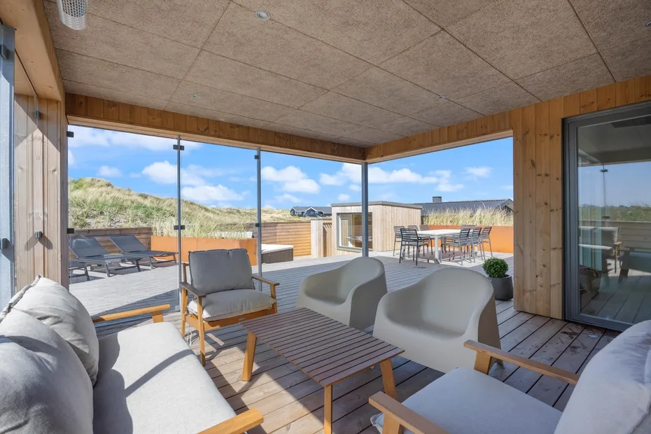 Una sala luminosa se abre a una terraza amueblada con asientos exteriores y amplias vistas del paisaje.