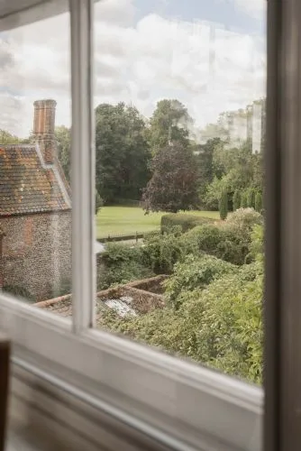 Vista de un jardín a través de una ventana, con árboles, setos y césped.