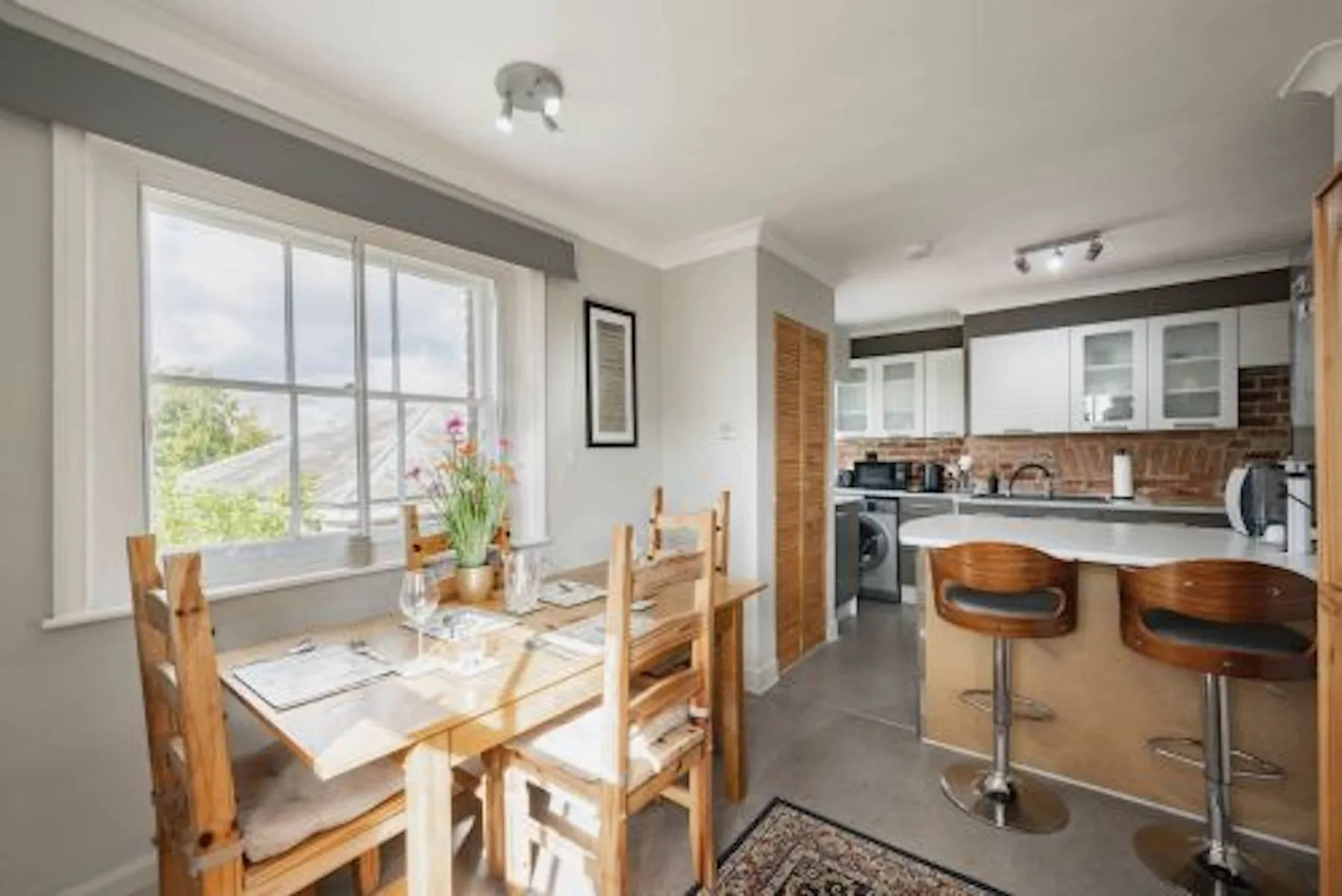 Un comedor junto a una cocina abierta, con una ventana amplia con vistas a la vegetación.