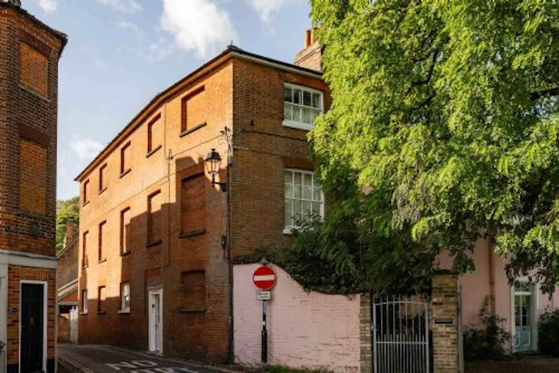Un edificio de ladrillo está junto a un árbol frondoso y un muro claro.