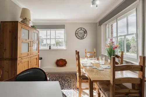 Un comedor luminoso con una mesa de madera junto a grandes ventanas.