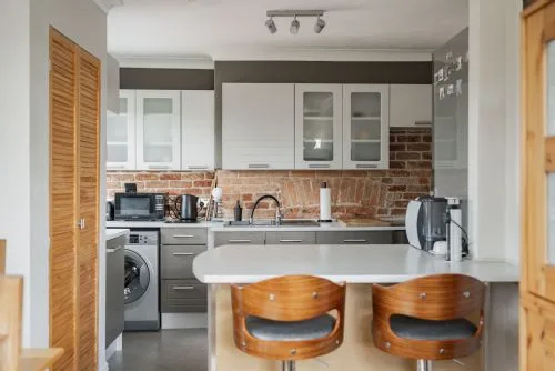 Una cocina luminosa con una isla central y dos taburetes de madera.