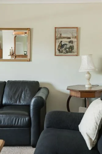 Una sala de estar con asientos oscuros, una mesa auxiliar y cuadros en la pared.