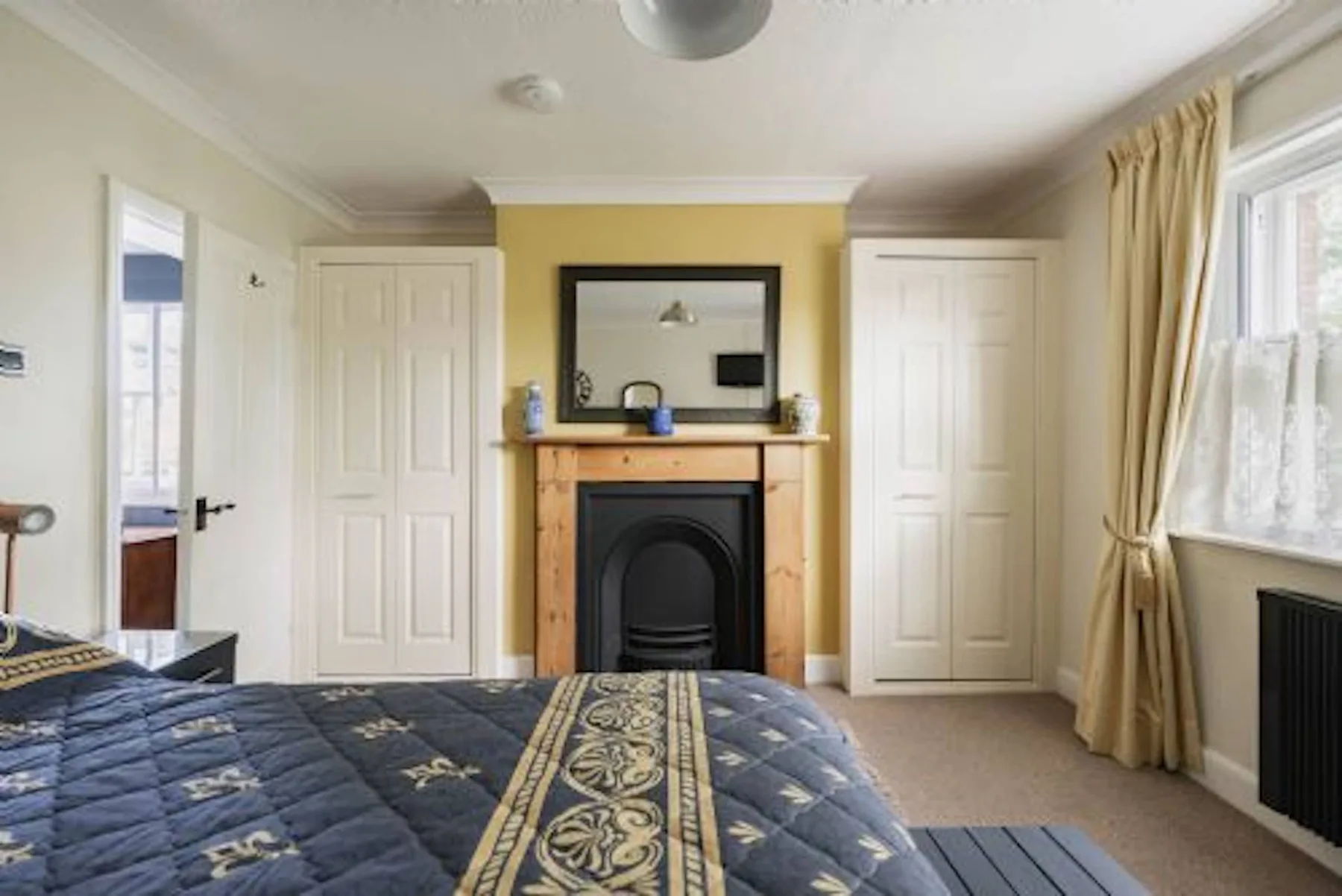 Un dormitorio con una cama, una chimenea y puertas en la pared del fondo.