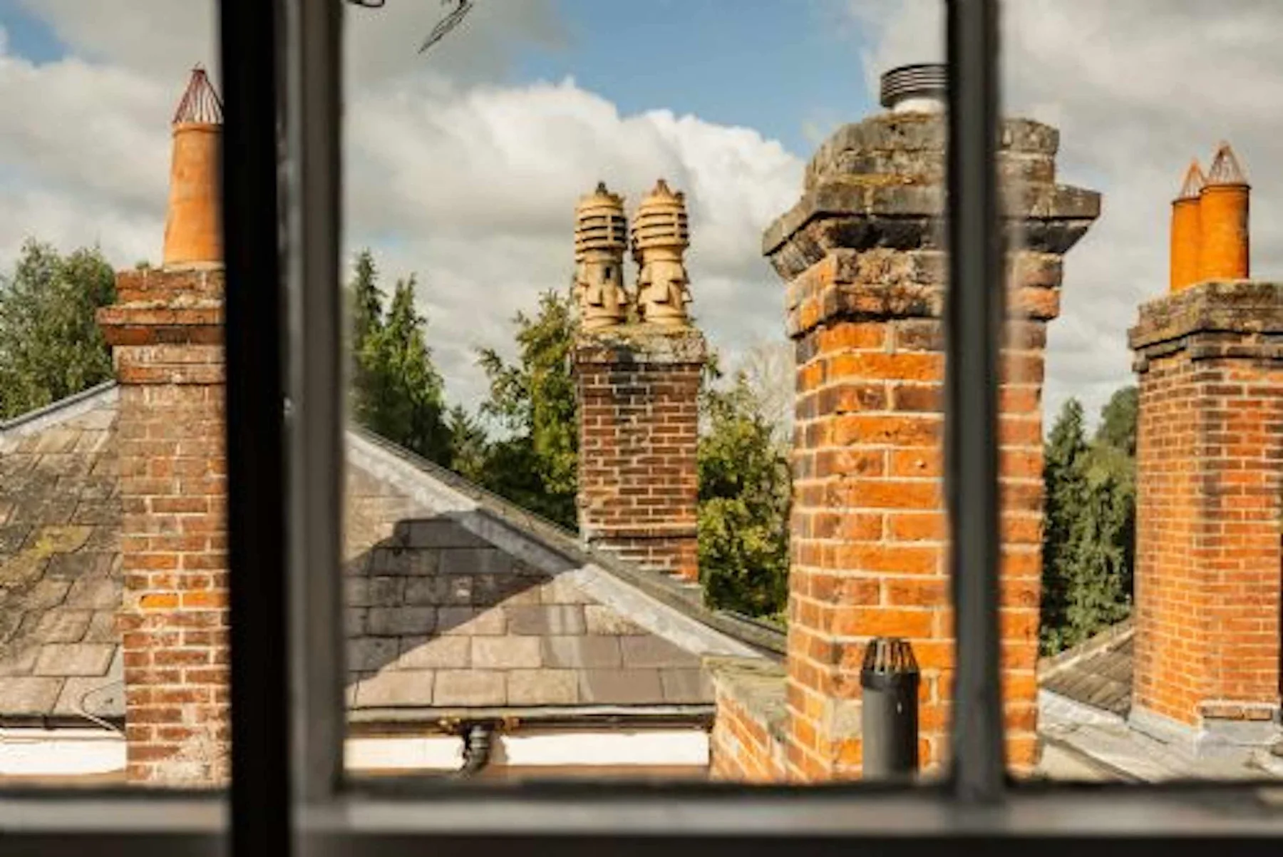 Una vista a través de una ventana muestra chimeneas de ladrillo sobre tejados cercanos.