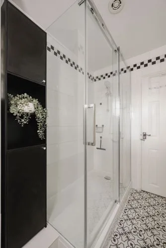 Un baño alicatado con ducha de vidrio y suelo estampado.
