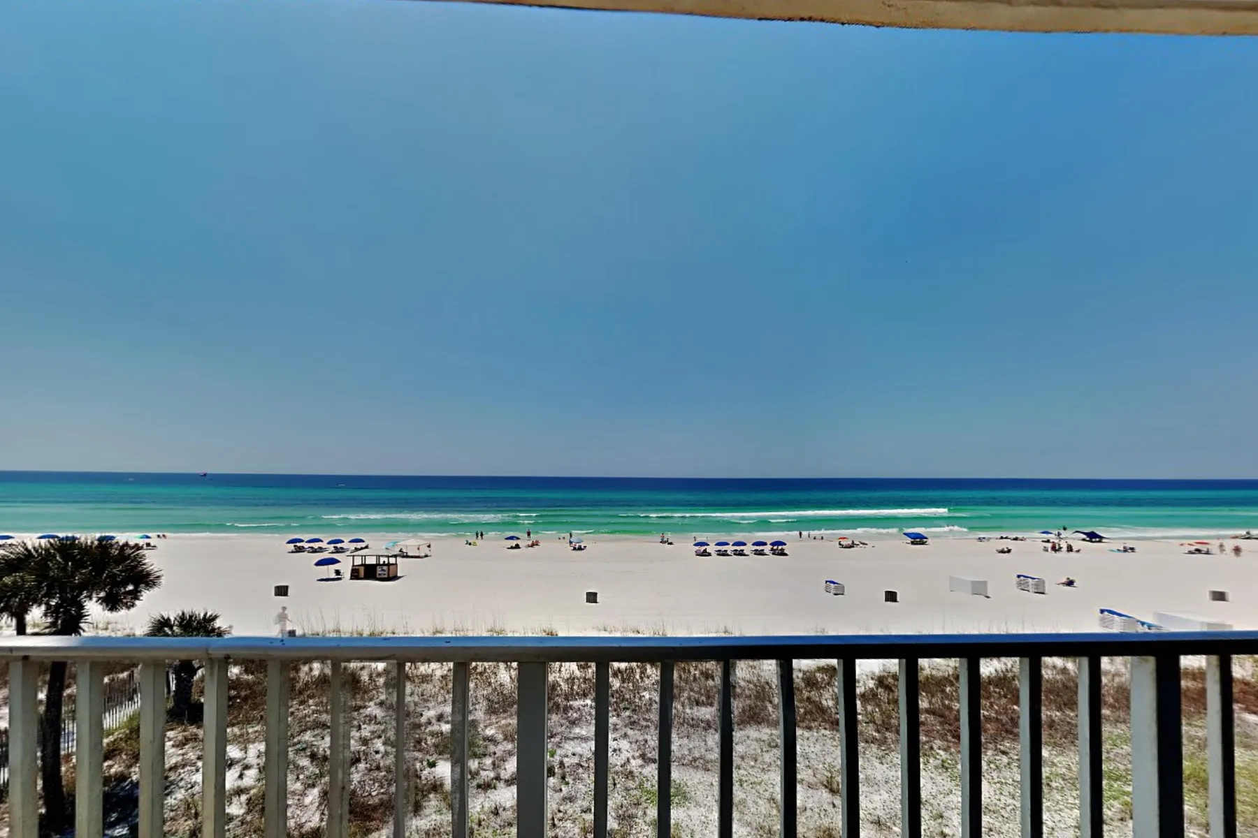 A beach viewed from a balcony, with rows of umbrellas along the shore.