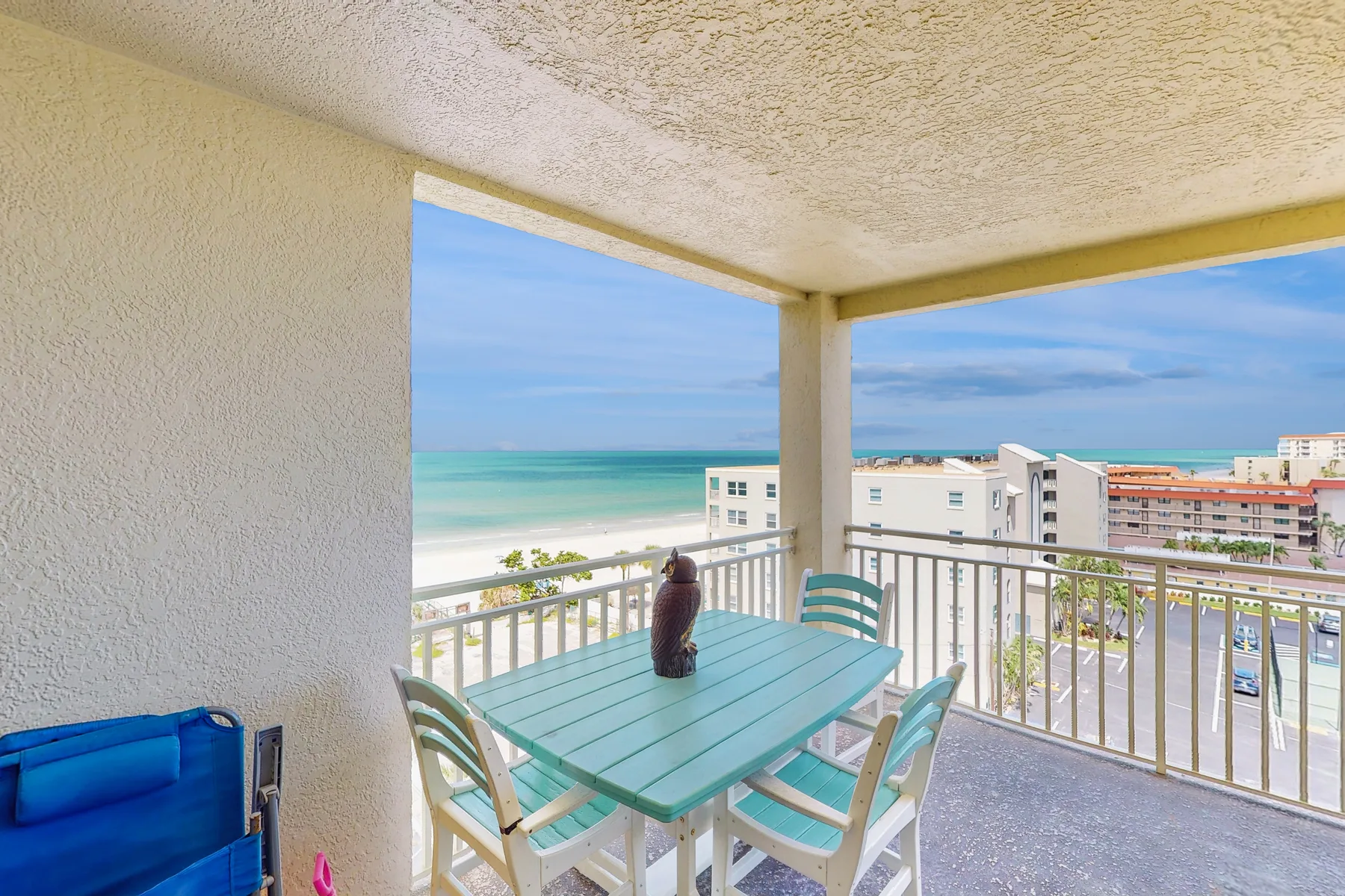 A covered balcony with turquoise seating overlooks the ocean and nearby buildings.