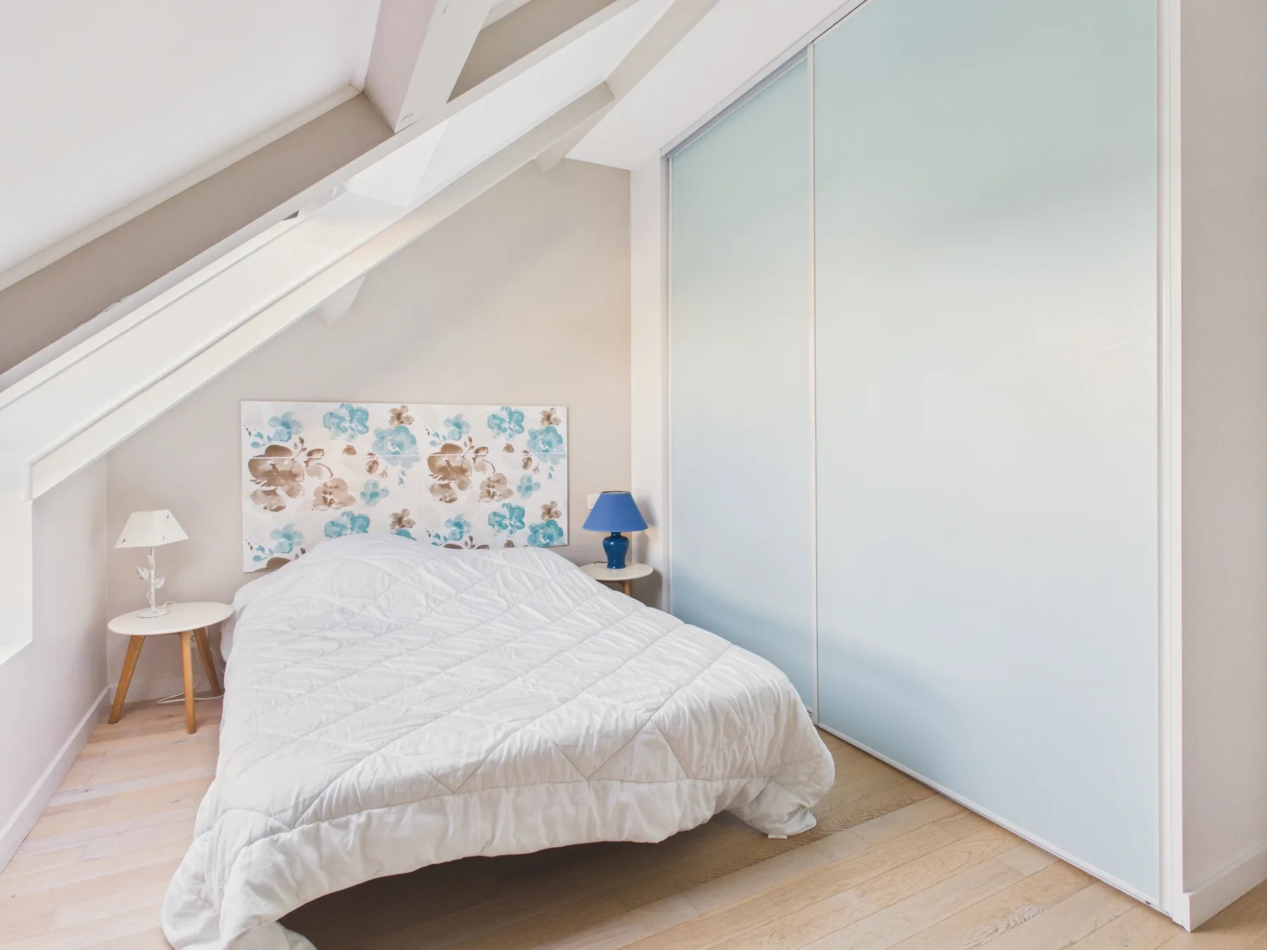 Un dormitorio con una cama bajo un techo inclinado y paneles claros.