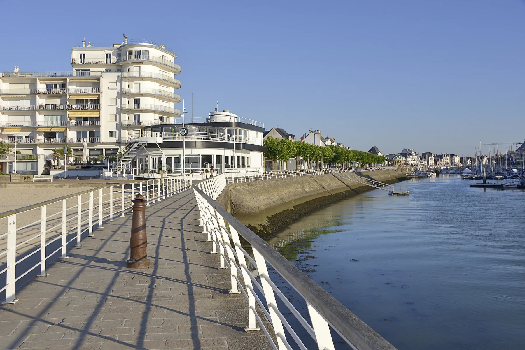 Un paseo marítimo bordea una marina junto a edificios modernos.
