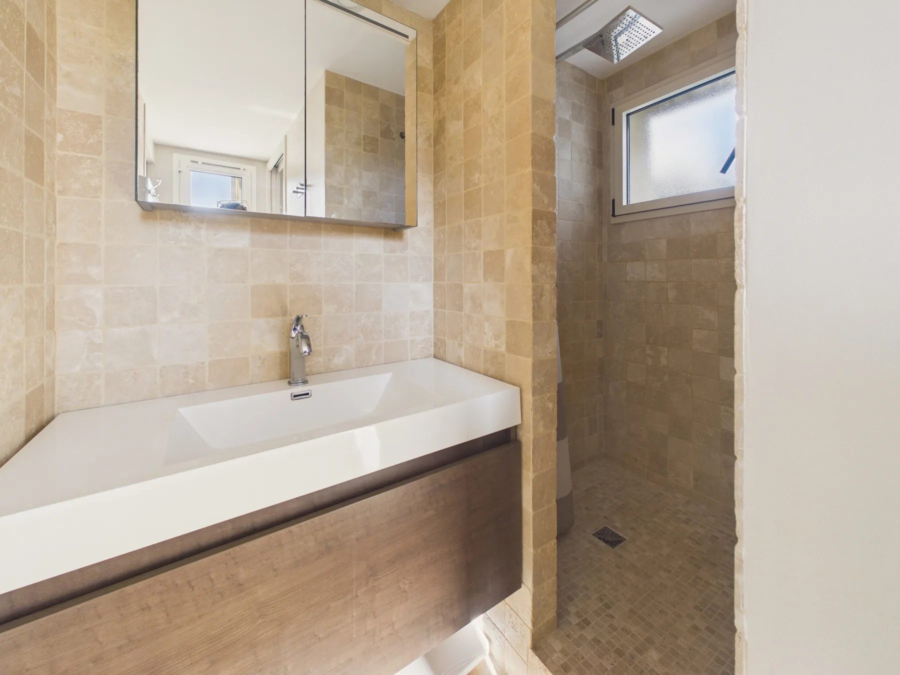 Un baño con azulejos, un lavabo alargado y una zona de ducha separada.