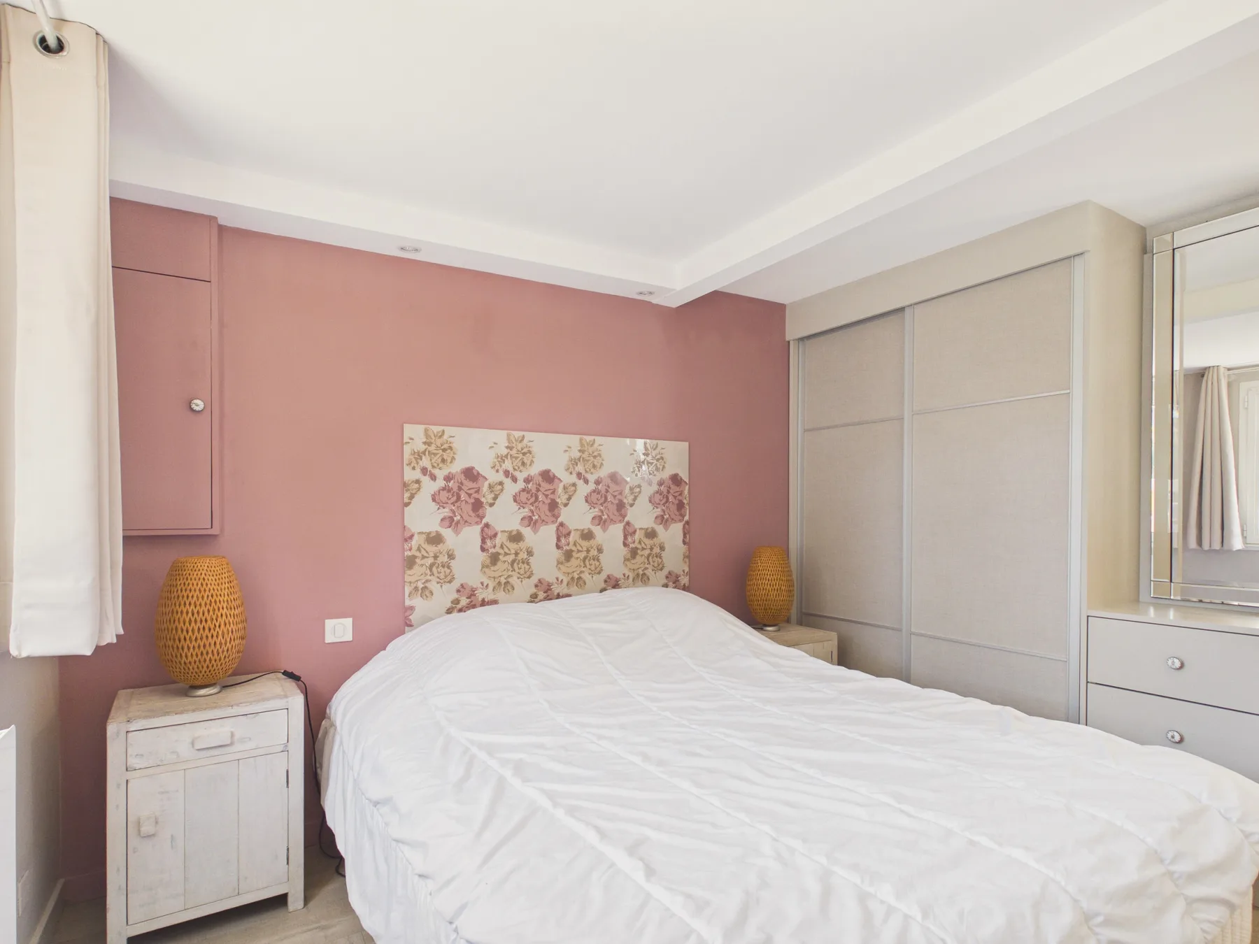 Dormitorio con una cama blanca junto a una pared rosa.