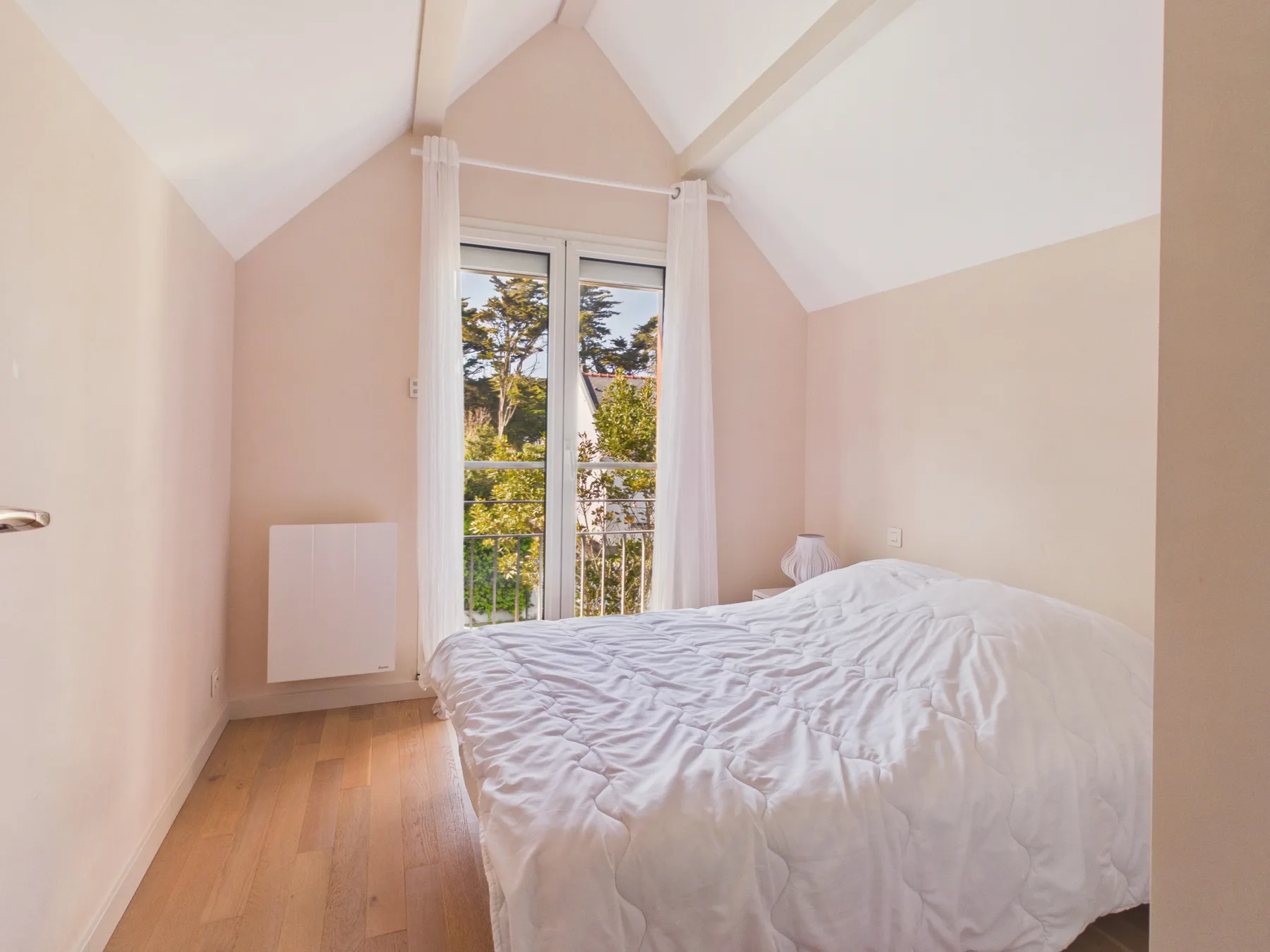 Un dormitorio luminoso con una cama junto a puertas de vidrio que dan a un balcón.