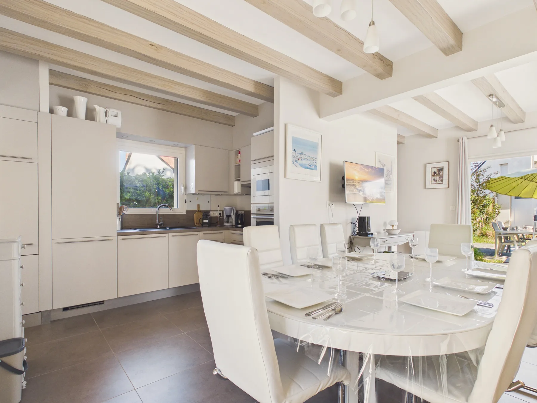 Una cocina y comedor luminosos con armarios blancos y una mesa de vidrio.