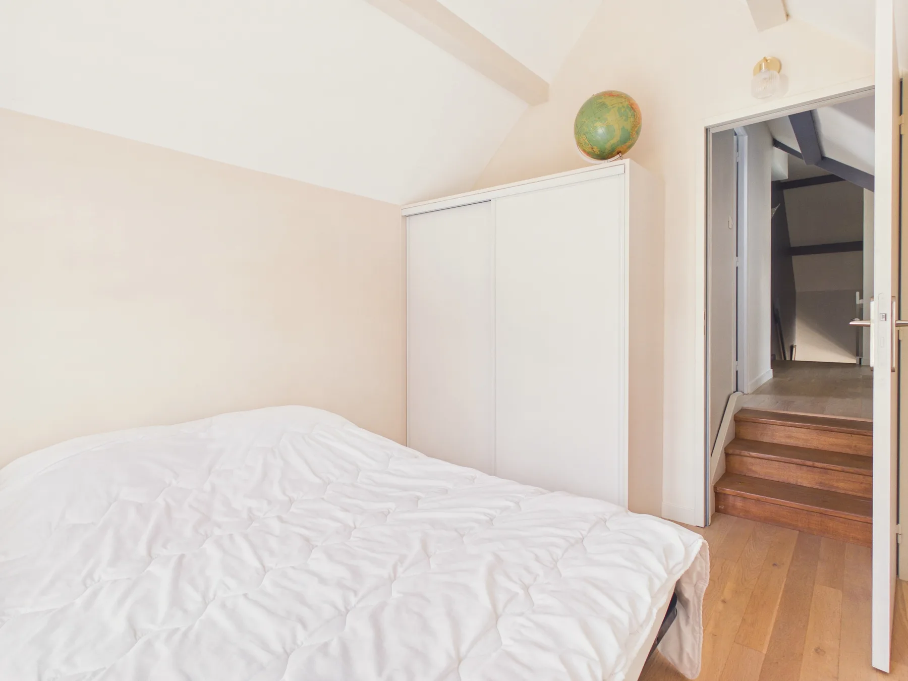 Un dormitorio con una cama blanca y un armario junto a una puerta abierta.